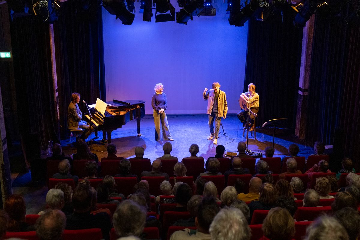4 artiesten voor blauwe achtergrond gezien vanuit de zaal