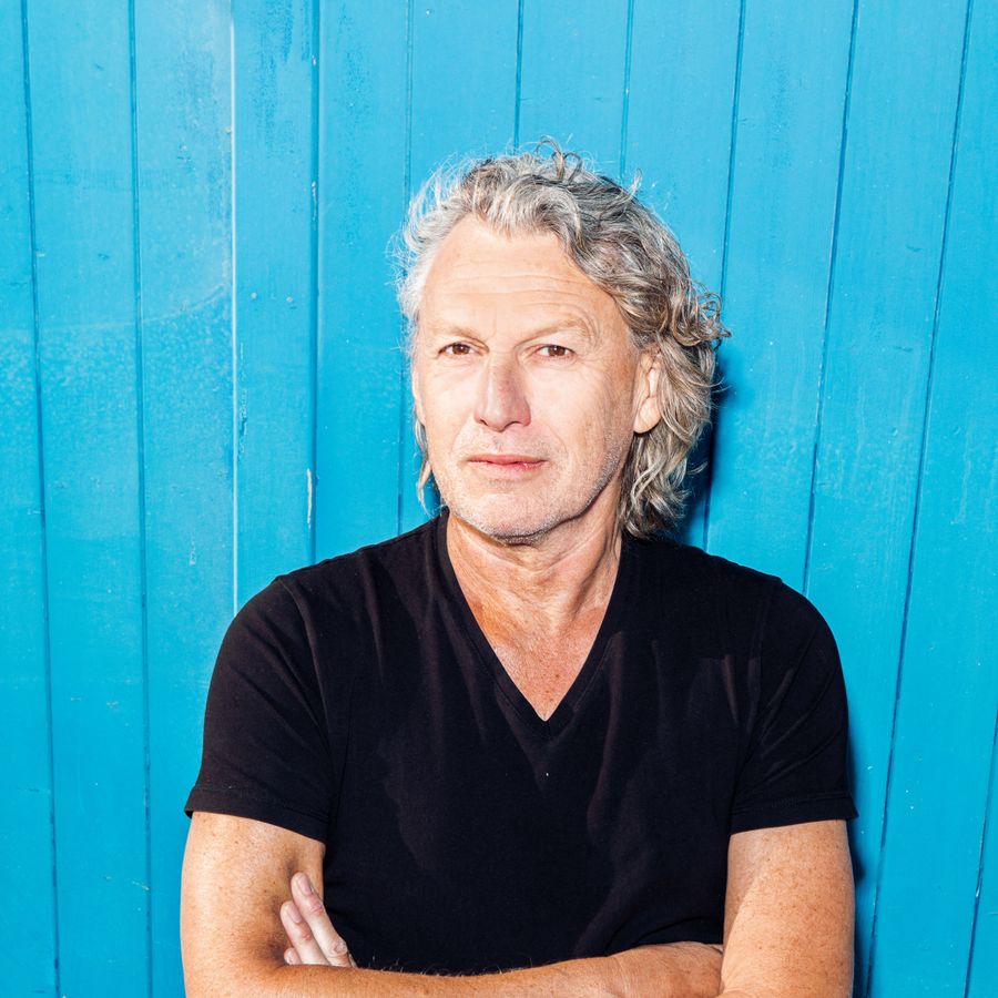 Edwin Winkels voor een felblauwe muur. Hij heeft zijn armen over elkaar