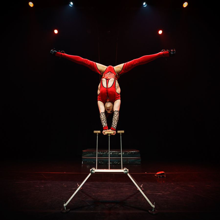 Acrobaat in rood pak voert wijdbeense handstand uit
