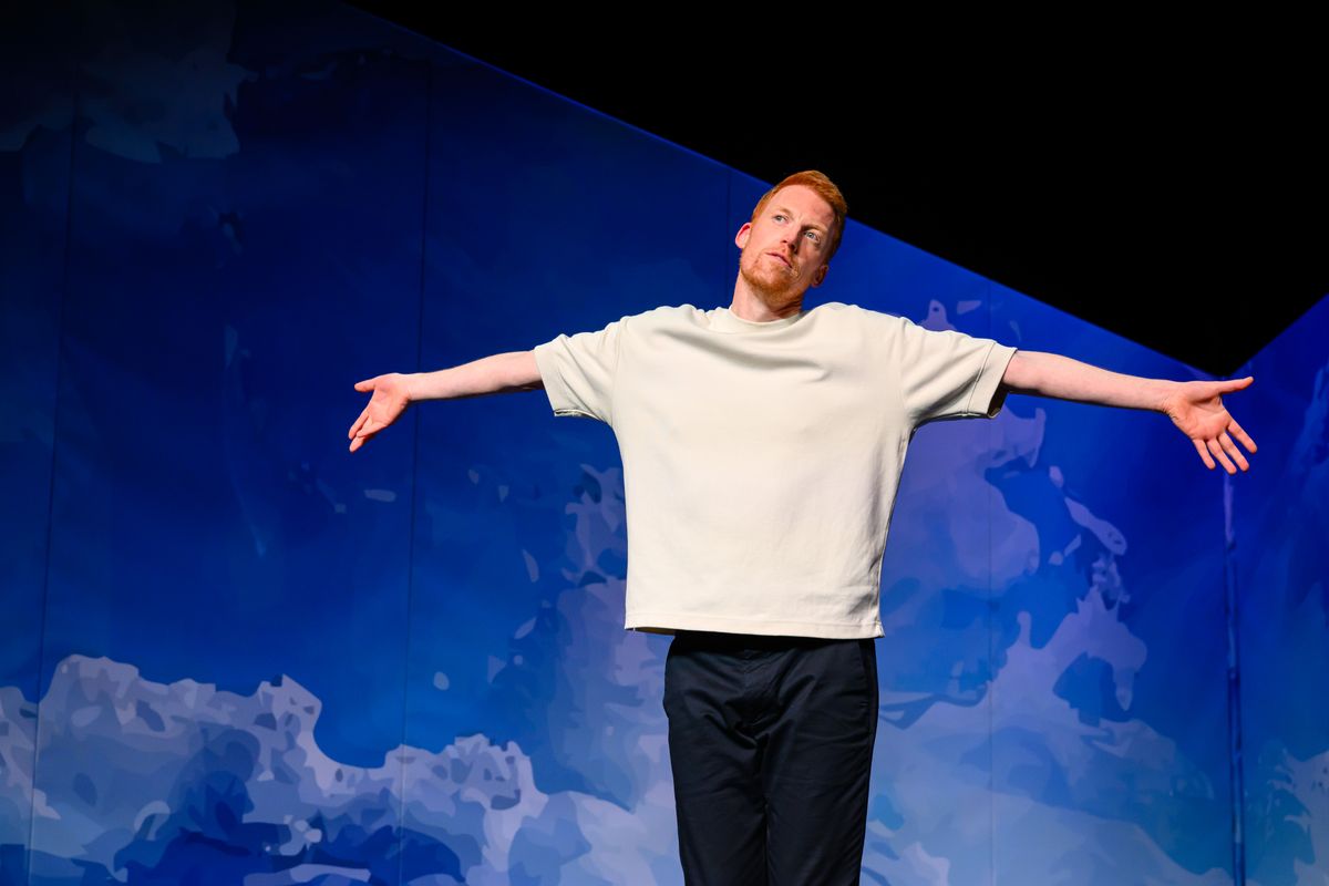 Rene van Meurs staat met zijn armen wijd voor een blauwe achtergrond