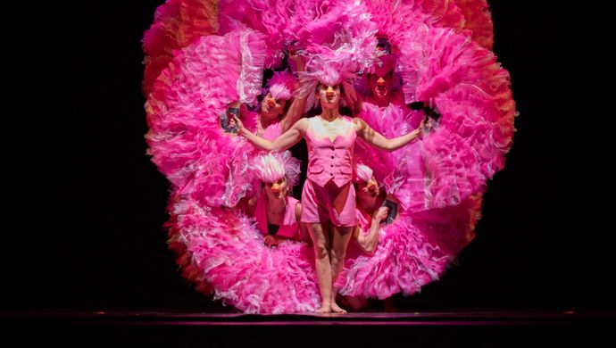 Dansers voor een zwarte achtergrond met roze doeken, ze beelden een flamingo uit