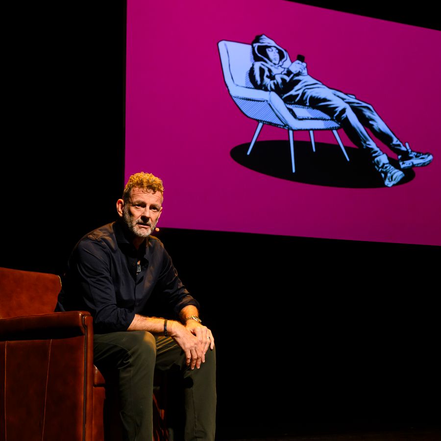 Kluun zit op een stoel voor een scherm met daarop een illustratie van en hangende puber op een stoel