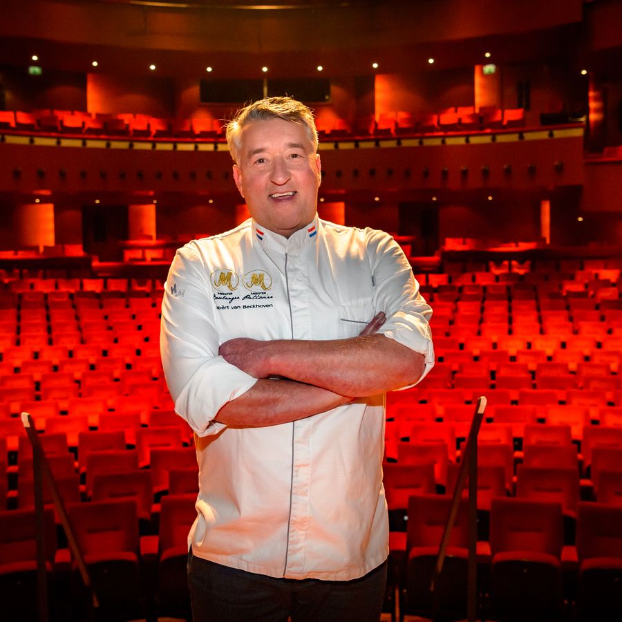 Robèrt van Beckhoven voor een lege theaterzaal. Hij draagt een kokshemd.