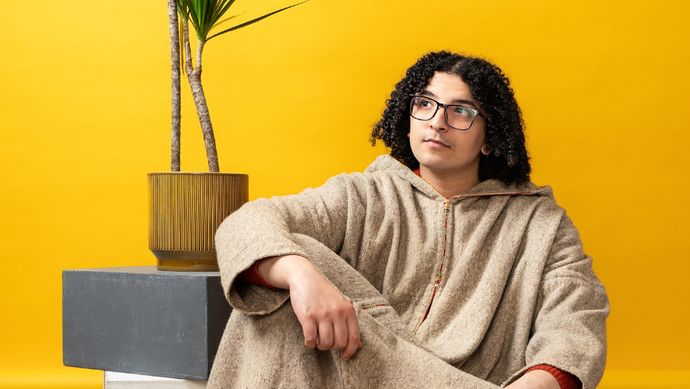 Ayoub zittend tegen een gele achtergrond