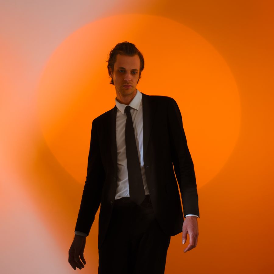 David Linszen in zwart pak voor een oranje achtergrond