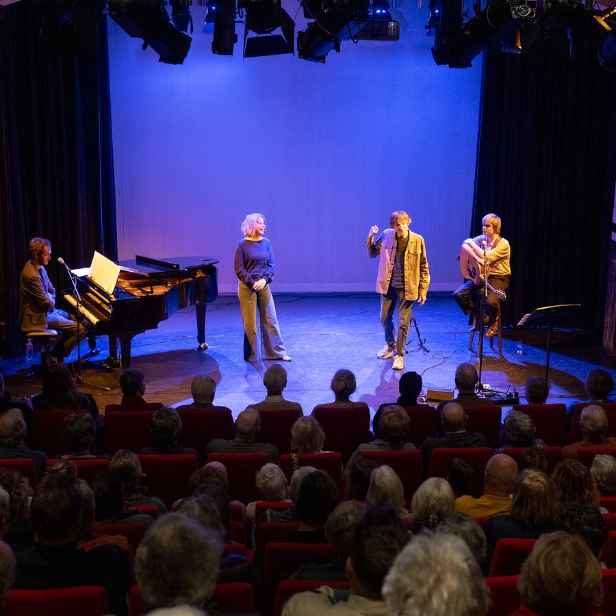 4 artiesten voor blauwe achtergrond gezien vanuit de zaal