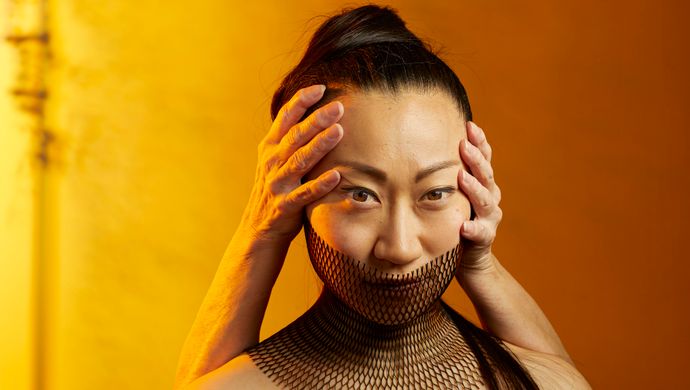 Danser met twee handen op haar hoofd. Gele achtergrond.