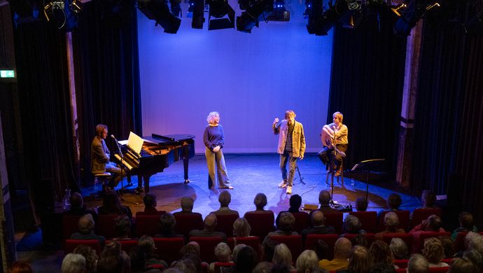 4 artiesten voor blauwe achtergrond gezien vanuit de zaal