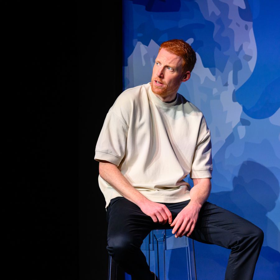 Rene van Meurs zit op een kruk voor een blauwe achtergrond