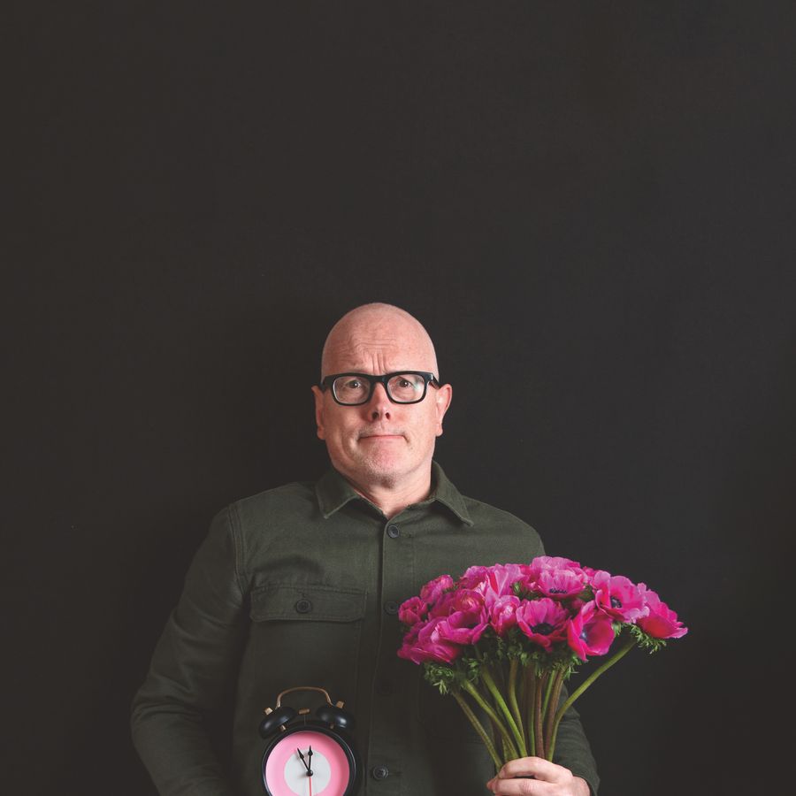 Kees van Amstel met in zijn rechterhand een bos roze bloemen en in zijn linkerhand een roze klok