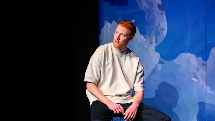 Rene van Meurs zit op een kruk voor een blauwe achtergrond