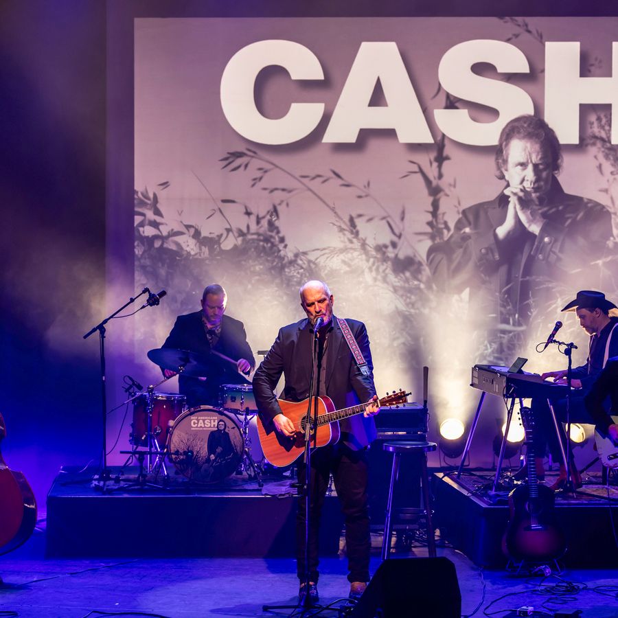 Muzikanten op podium metop achtergrond foto van Johnny Cash