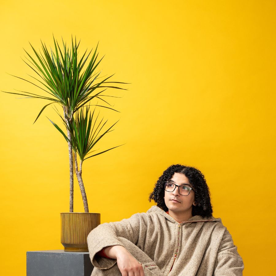 Ayoub zittend tegen een gele achtergrond