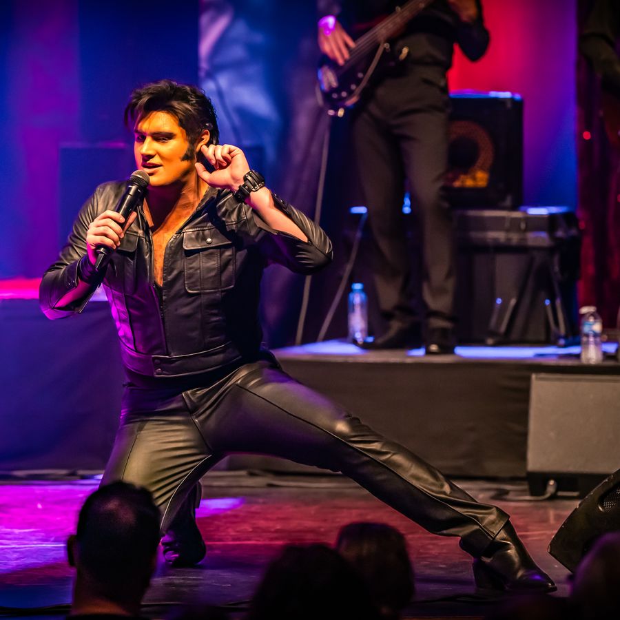 Zanger verkleed als Elvis Presley zit met een knie op de grond en het andere been uitgestrekt naast hem