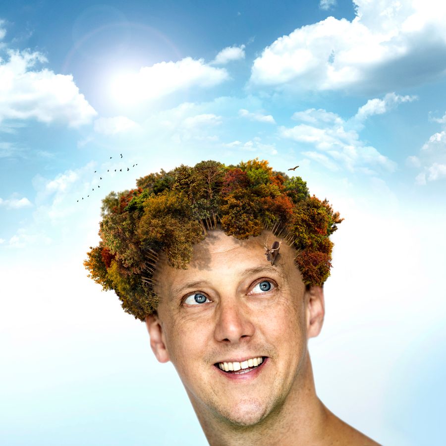Jochem Myjer voor een blauwe lucht met wolkjes en zijn haren zijn een bos